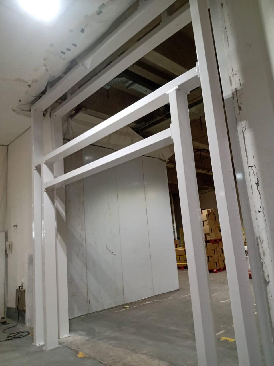 Estrutura branca com colunas e travessas junto a uma passagem industrial